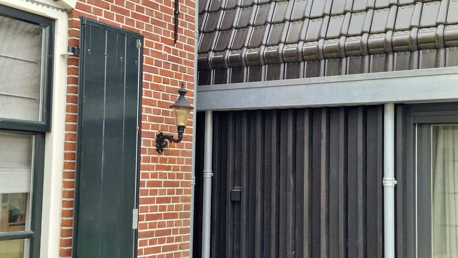 Overgang tussen bestaand metselwerk en nieuw houten volume bij het bijgebouw.